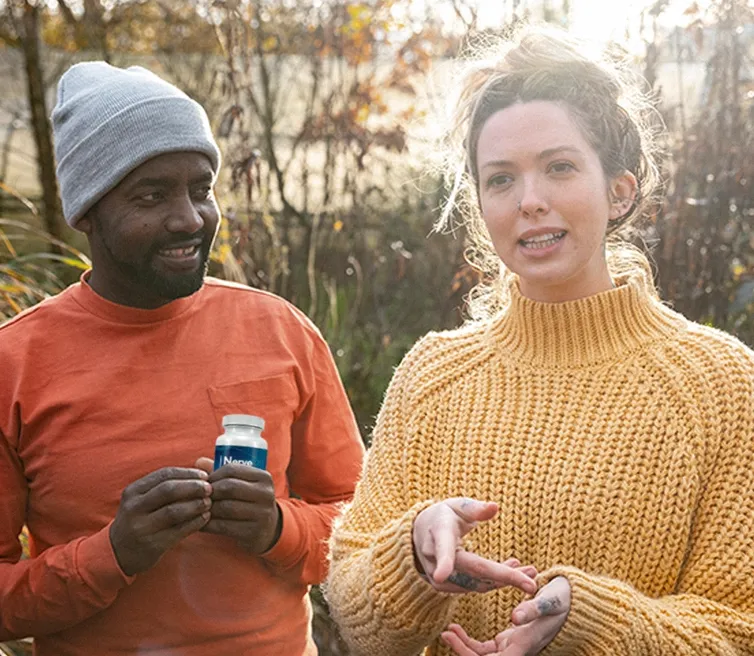 A couple smiling outdoors, one holding a supplement bottle